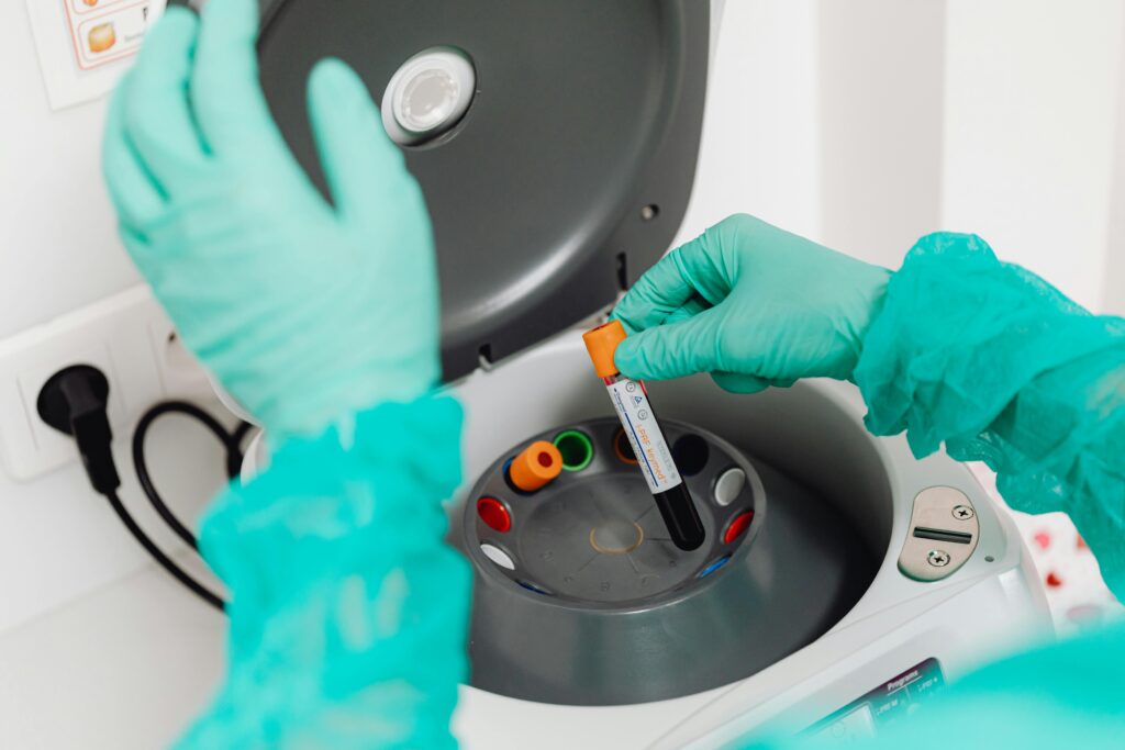 A lab technician wearing gloves uses a centrifuge for blood analysis in a modern laboratory setting.